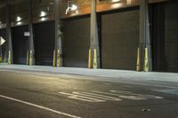 two people walking along the sidewalk next to a bus stop sign and garage doors on the side of a city street