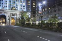 a car drives on a city street under lighted buildings at night with a clock tower