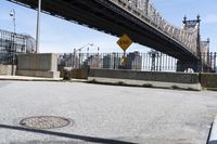 there is a manhole on the curb of the street in front of the bridge