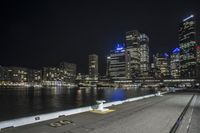 a city skyline and street lights shining from above, with a body of water running beside