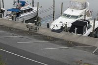 two boats docked in a marina on the water near cars and poles for transportation with a skylight above them