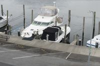 two boats docked in a marina on the water near cars and poles for transportation with a skylight above them