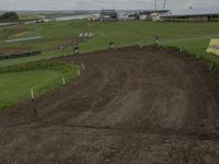 a dirt bike track being built on top of a hill in a field with buildings behind it