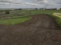 a dirt bike track being built on top of a hill in a field with buildings behind it