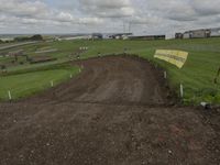 a dirt bike track being built on top of a hill in a field with buildings behind it