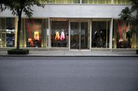 a store front with mannequins hanging from the glass windows and a tree
