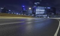 an empty highway leads into a city at night near skyscrapers and road lamps in the distance