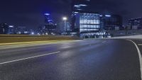 an empty highway leads into a city at night near skyscrapers and road lamps in the distance