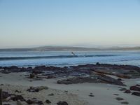 three people on surfboards near some water and rocks in the sand with mountains in the background