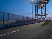 a very large metal bridge over a highway with lights on it's side at dusk