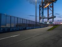 a very large metal bridge over a highway with lights on it's side at dusk