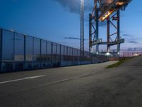 a very large metal bridge over a highway with lights on it's side at dusk