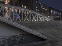 a view of a metal pedestrian bridge over water on the street at night with buildings behind it