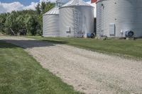 two metal silos are seen next to each other on the side of an empty dirt road