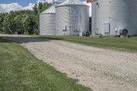 two metal silos are seen next to each other on the side of an empty dirt road