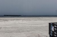 large metal structure behind a sandy area under cloudy skies of overcast sky and ocean