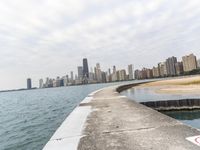 a long concrete pier has water on it near the city skyline on the ocean and skyscrapers