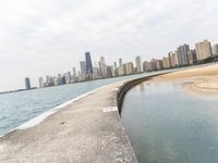 a long concrete pier has water on it near the city skyline on the ocean and skyscrapers