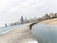 a long concrete pier has water on it near the city skyline on the ocean and skyscrapers