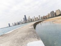 a long concrete pier has water on it near the city skyline on the ocean and skyscrapers