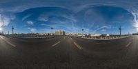 fisheye lens picture of curved roadway with sky and clouds in the background by a pier