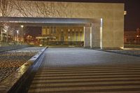 an empty walkway with lit up building in the background and water feature at the bottom of it