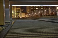 an empty walkway with lit up building in the background and water feature at the bottom of it