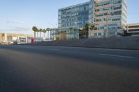 a car drives on an empty road and towards some buildings and palm trees in the background