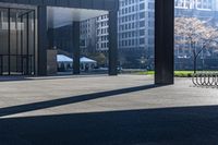 a long bench on concrete surrounded by tall buildings in a big city parking lot with blue sky