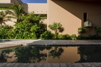 an empty pool in front of a tan building with small windows on it, and lush vegetation around