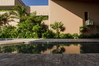 an empty pool in front of a tan building with small windows on it, and lush vegetation around