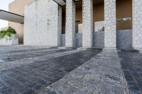 an empty stone walk way in front of some white buildings with stone flooring and gray pillars