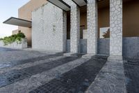 an empty stone walk way in front of some white buildings with stone flooring and gray pillars