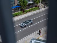 a woman walking by a silver car on the road by a sidewalk and cars parked along the street