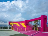 a basketball court painted in a pink, yellow and blue design with stairs up to the roof