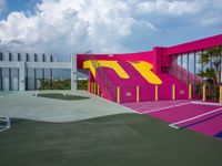 a basketball court painted in a pink, yellow and blue design with stairs up to the roof