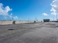 empty parking lot with blue sky and clouds behind it and traffic lights and utility post