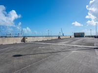 empty parking lot with blue sky and clouds behind it and traffic lights and utility post