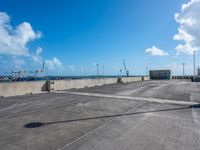 empty parking lot with blue sky and clouds behind it and traffic lights and utility post