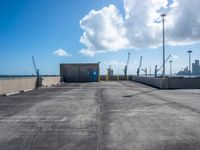 an empty parking lot with some concrete and a sky background and a blue door with white clouds above