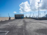 an empty parking lot with some concrete and a sky background and a blue door with white clouds above