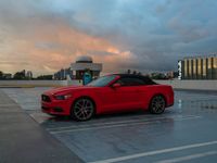 a red sports car parked at an airport parking lot with clouds in the background,