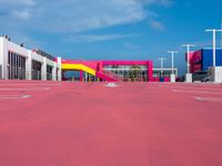 a large building with a very colorful entrance way next to a big pink gate and some street lamps