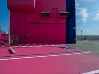 there is a parking lot with a pink building in the background and a blue building