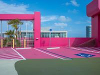 a basketball court on a bright pink building with white windows and a parking lot area