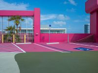 a basketball court on a bright pink building with white windows and a parking lot area