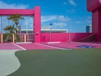 a basketball court on a bright pink building with white windows and a parking lot area