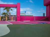 a basketball court on a bright pink building with white windows and a parking lot area