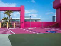 a basketball court on a bright pink building with white windows and a parking lot area