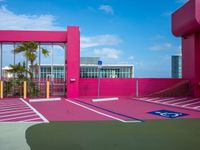 a basketball court on a bright pink building with white windows and a parking lot area